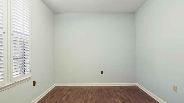 empty room featuring dark wood-type flooring and baseboards