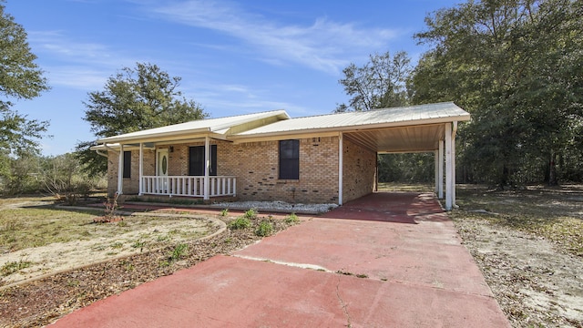 ranch-style home featuring a carport, covered porch, brick siding, and metal roof