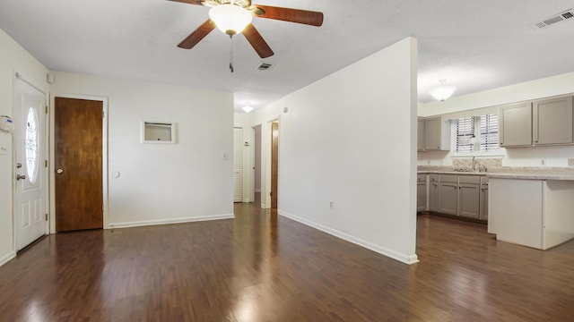 unfurnished living room with baseboards, visible vents, dark wood-style flooring, and a sink