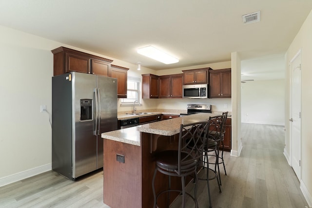 kitchen with sink, a center island, light hardwood / wood-style floors, a breakfast bar area, and appliances with stainless steel finishes