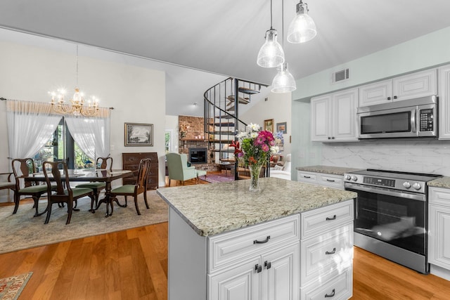 kitchen featuring appliances with stainless steel finishes, light wood-type flooring, a brick fireplace, decorative light fixtures, and a kitchen island