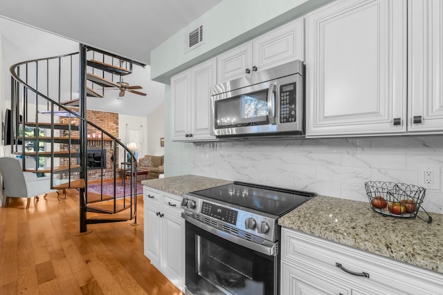 kitchen with light stone counters, backsplash, light hardwood / wood-style floors, white cabinets, and appliances with stainless steel finishes