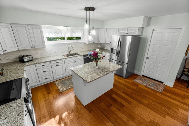 kitchen with appliances with stainless steel finishes, sink, decorative light fixtures, white cabinetry, and a kitchen island