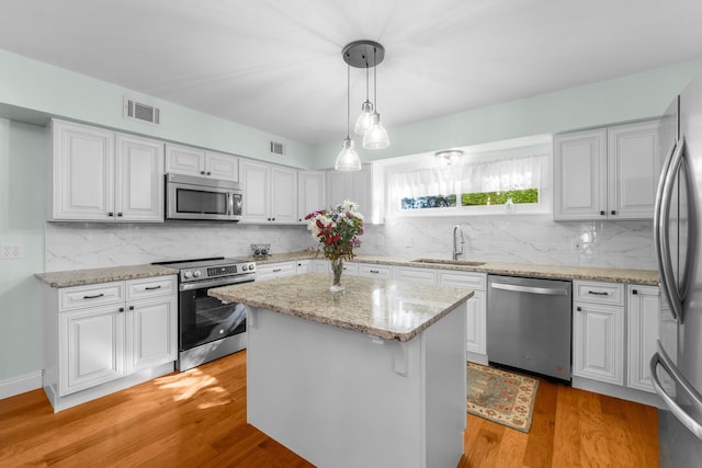 kitchen with stainless steel appliances, sink, a center island, white cabinetry, and hanging light fixtures