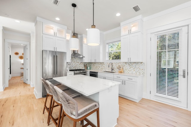 kitchen with white cabinetry, sink, hanging light fixtures, stainless steel appliances, and a kitchen island