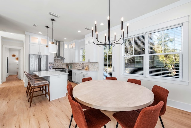 dining space featuring light wood-type flooring, a notable chandelier, a healthy amount of sunlight, and sink