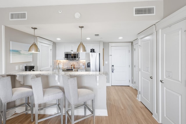 kitchen featuring white cabinetry, stainless steel appliances, pendant lighting, a kitchen bar, and light wood-type flooring