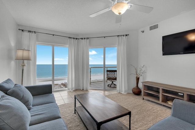 tiled living room with a beach view, a textured ceiling, a water view, and ceiling fan