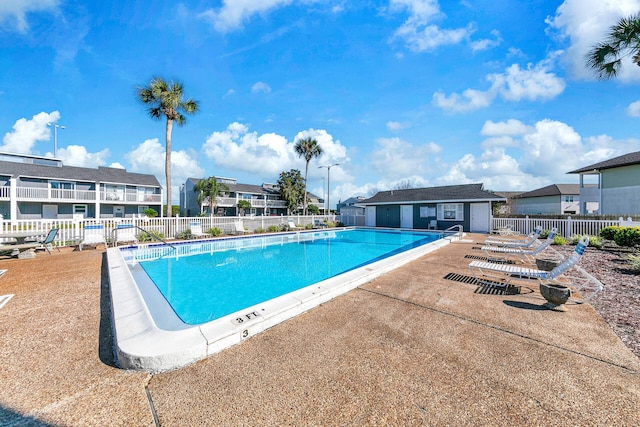 pool with a patio area, a residential view, fence, and an outbuilding