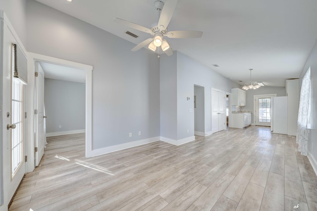 unfurnished living room with washer / dryer, ceiling fan with notable chandelier, light hardwood / wood-style floors, and vaulted ceiling