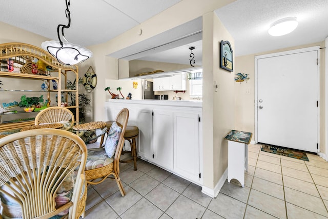 kitchen featuring decorative light fixtures, light tile patterned flooring, white cabinetry, and stainless steel refrigerator