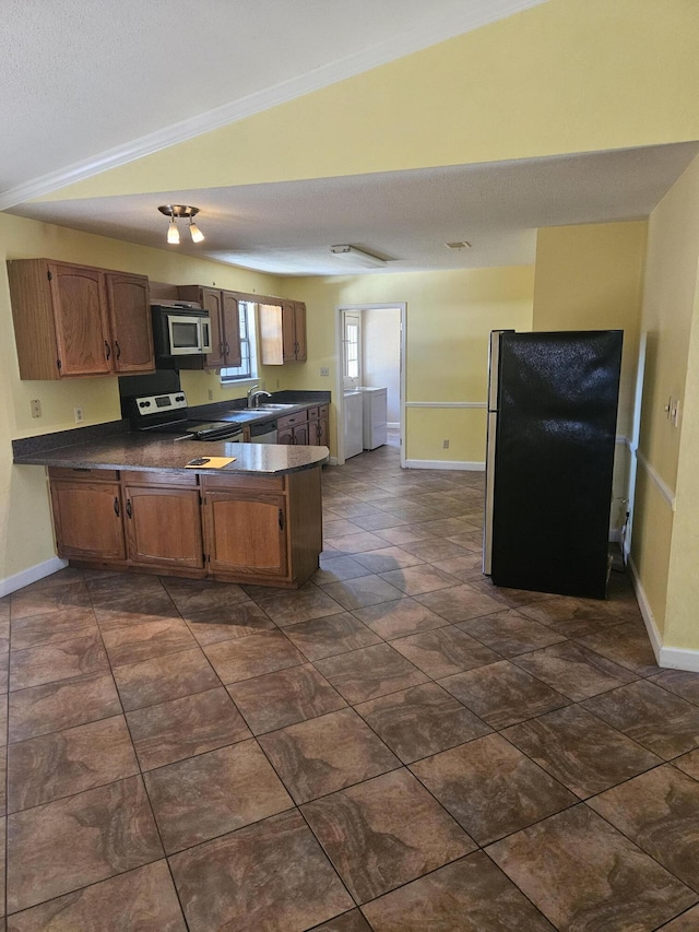 kitchen featuring washing machine and dryer, kitchen peninsula, lofted ceiling, black refrigerator, and range