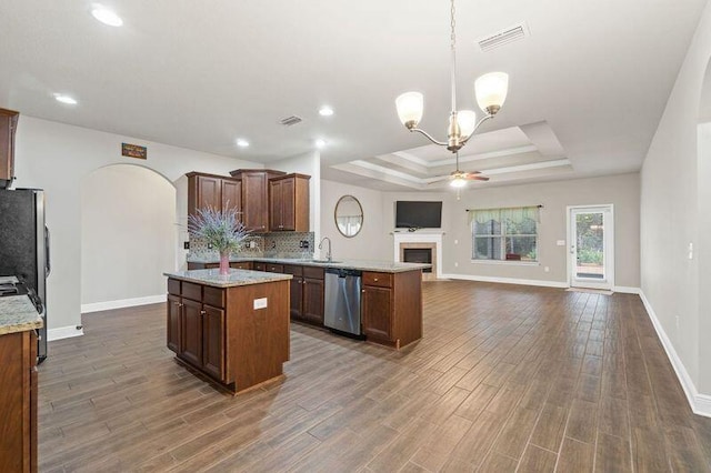 kitchen with a center island, dark wood-type flooring, a raised ceiling, appliances with stainless steel finishes, and decorative light fixtures