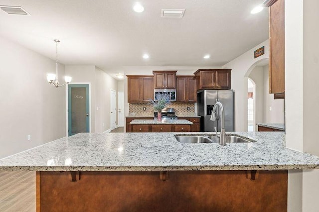 kitchen featuring an inviting chandelier, sink, appliances with stainless steel finishes, light stone counters, and kitchen peninsula