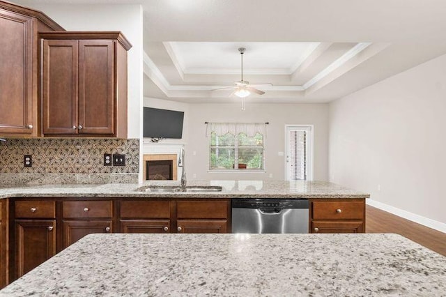 kitchen with light stone counters, a raised ceiling, ceiling fan, sink, and dishwasher