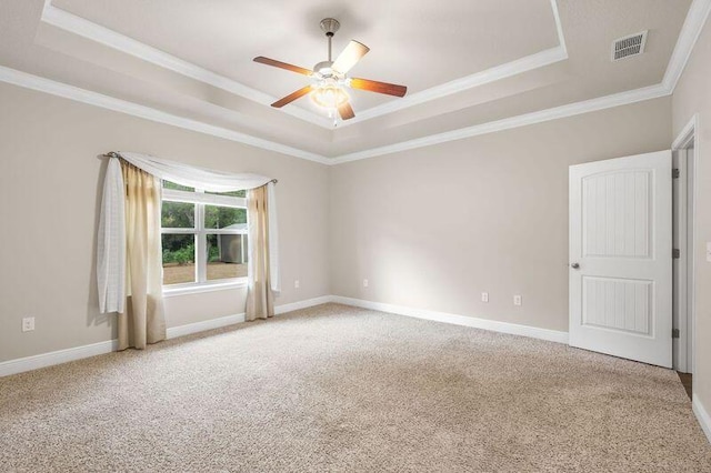 empty room featuring a tray ceiling, ceiling fan, crown molding, and light colored carpet