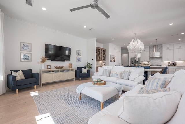 living room with ceiling fan with notable chandelier, light hardwood / wood-style flooring, and ornamental molding