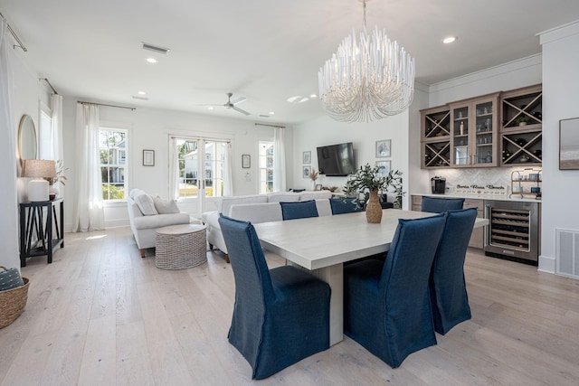 dining space with ceiling fan with notable chandelier, bar area, beverage cooler, and light wood-type flooring