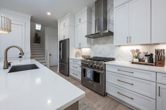 kitchen with sink, hanging light fixtures, high quality appliances, wall chimney range hood, and white cabinets