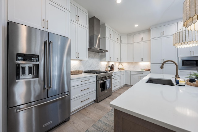 kitchen featuring sink, premium appliances, white cabinets, decorative light fixtures, and wall chimney exhaust hood