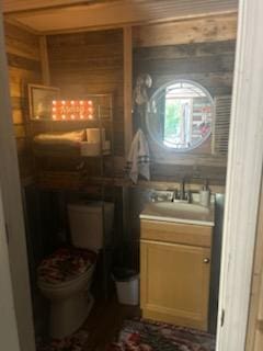 bathroom with vanity, toilet, and wood walls