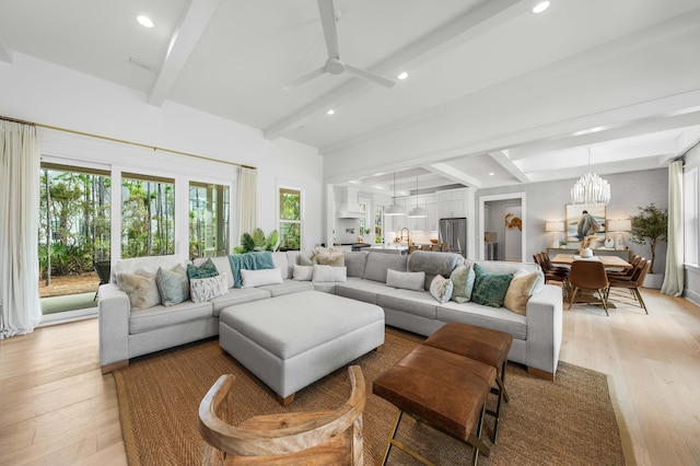 living room with light hardwood / wood-style floors, ceiling fan with notable chandelier, and beamed ceiling