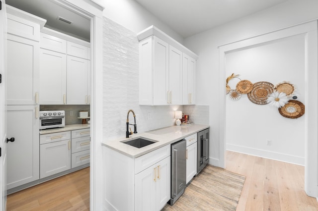 kitchen featuring sink, light hardwood / wood-style flooring, white cabinetry, wine cooler, and decorative backsplash