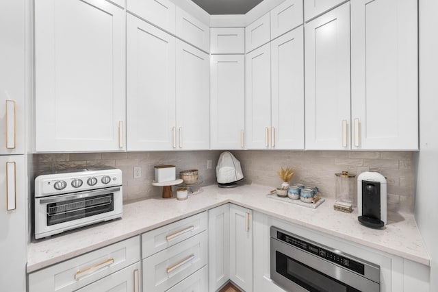 kitchen featuring light stone countertops, stainless steel microwave, white cabinets, and decorative backsplash