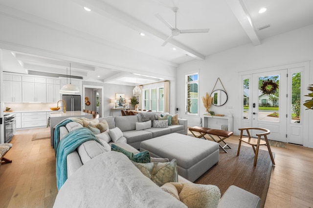 living room featuring sink, light wood-type flooring, ceiling fan, and beam ceiling