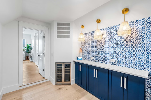 bar with blue cabinets, beverage cooler, pendant lighting, and light hardwood / wood-style floors