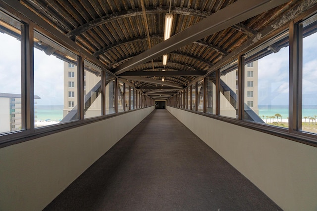 hall with carpet, a water view, and lofted ceiling with beams