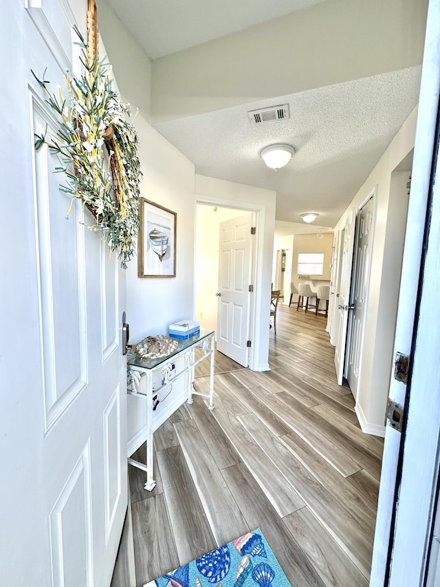 hall with light hardwood / wood-style floors and a textured ceiling