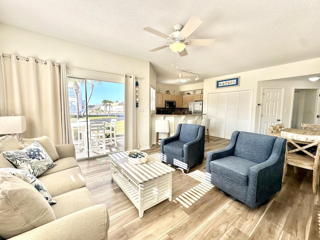 living room with a textured ceiling, light wood-type flooring, and ceiling fan