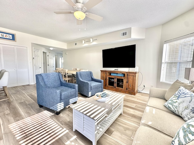 living room featuring ceiling fan, light hardwood / wood-style floors, and a textured ceiling