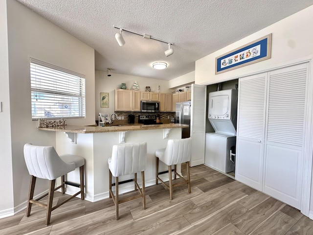 kitchen with a breakfast bar area, stacked washer and dryer, stainless steel appliances, and light hardwood / wood-style flooring