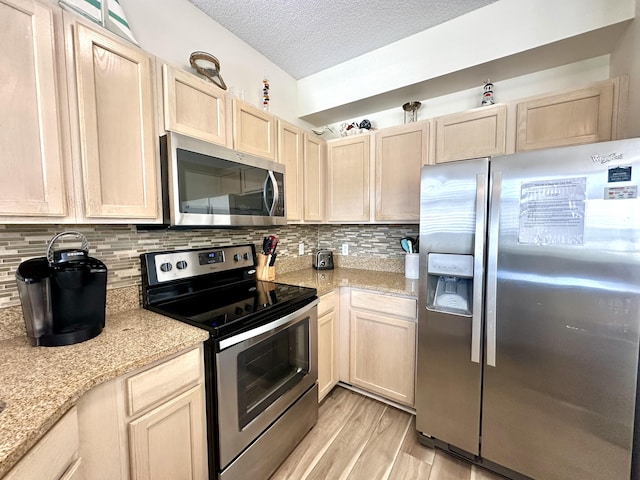 kitchen featuring light wood-type flooring, light brown cabinetry, a textured ceiling, and stainless steel appliances