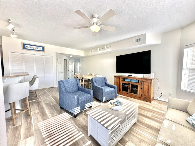 living room featuring a textured ceiling, light hardwood / wood-style flooring, and ceiling fan