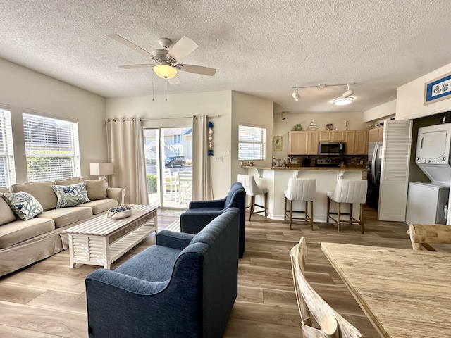 living room featuring a textured ceiling, ceiling fan, light hardwood / wood-style floors, and stacked washer and dryer