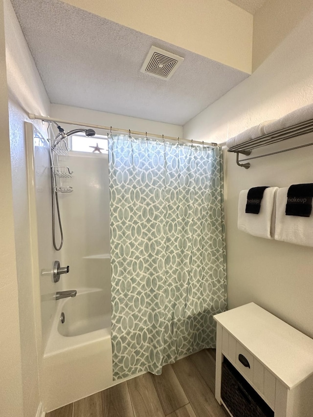 bathroom with hardwood / wood-style flooring, shower / bath combination with curtain, and a textured ceiling