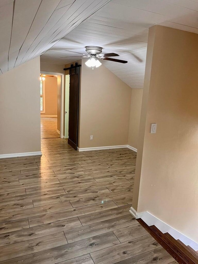 unfurnished room featuring wood-type flooring, a barn door, ceiling fan, and lofted ceiling