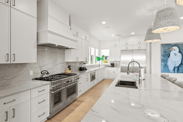 kitchen with pendant lighting, sink, white cabinetry, premium appliances, and custom range hood