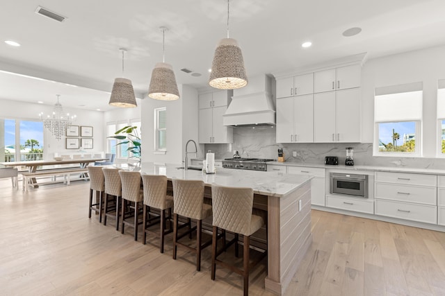 kitchen with a kitchen island with sink, white cabinetry, custom exhaust hood, and decorative light fixtures