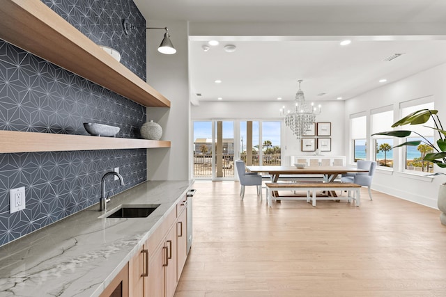 kitchen with sink, light hardwood / wood-style flooring, pendant lighting, light stone countertops, and backsplash