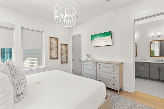 bedroom featuring ensuite bathroom, a chandelier, sink, and light hardwood / wood-style flooring