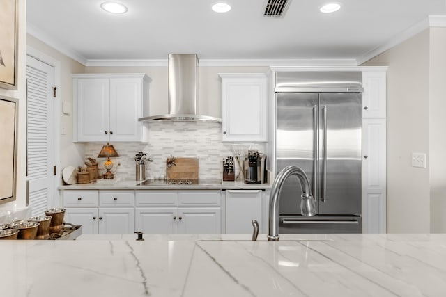 kitchen with white cabinets, light stone countertops, wall chimney range hood, and built in refrigerator