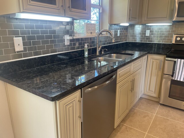 kitchen featuring backsplash, stainless steel appliances, sink, light tile patterned floors, and dark stone countertops