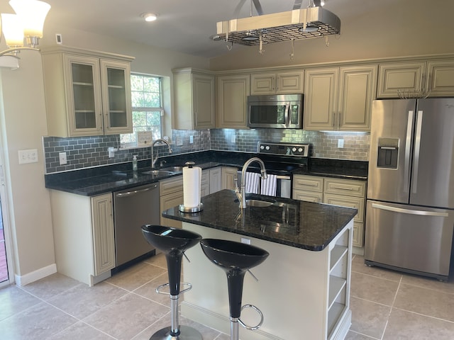 kitchen featuring stainless steel appliances, backsplash, an island with sink, dark stone counters, and light tile patterned floors