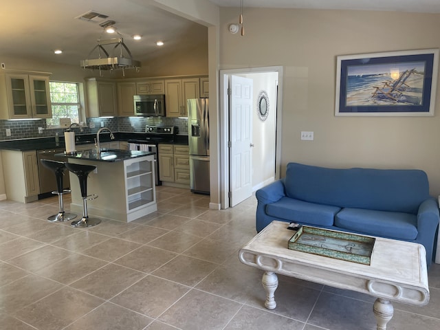 kitchen with appliances with stainless steel finishes, backsplash, a center island with sink, and vaulted ceiling