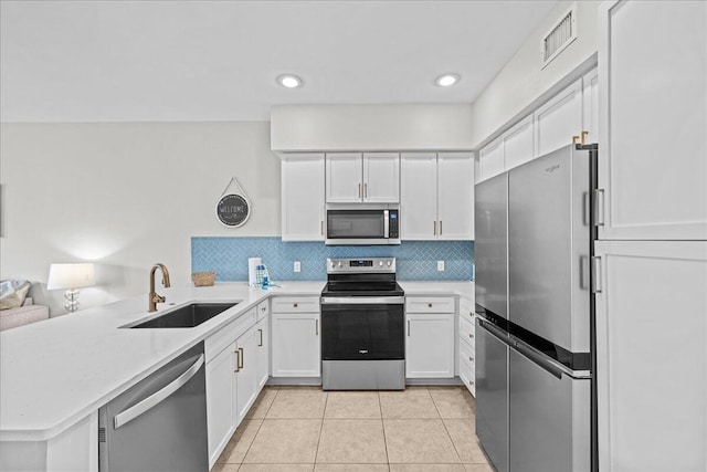 kitchen with sink, tasteful backsplash, kitchen peninsula, white cabinets, and appliances with stainless steel finishes