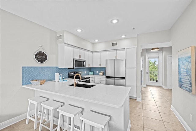 kitchen with kitchen peninsula, decorative backsplash, stainless steel appliances, sink, and white cabinetry